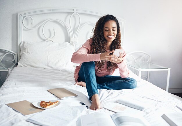 Books bed and woman with a phone reading social media and internet posts on break from studying in a bedroom Student learning and relax by black woman browsing online for idea for creative writing