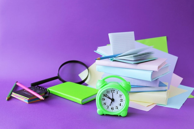 Books a magnifying glass an alarm clock and notepads on the table