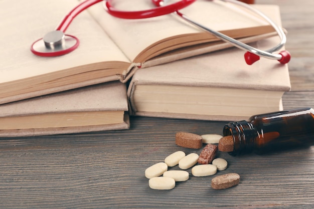 Books pills and stethoscope on wooden table closeup