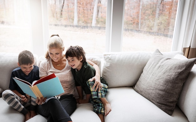 Books reading and mother with kids on sofa for storytelling time in living room of happy home Love learning and woman with children book and fantasy story on couch growth and child development