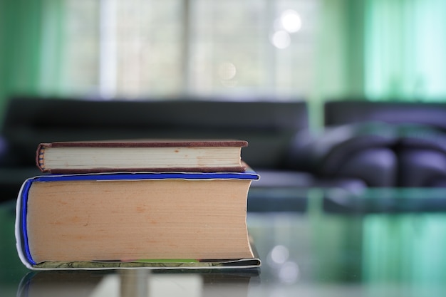 books stack on top glass table with blur sofa set in living room background