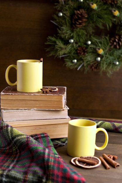 Books and two yellow cups near wreath with cinnamon near christmas decorations on wooden table