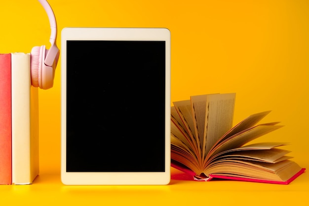 Books with digital tablet and headphones on yellow background