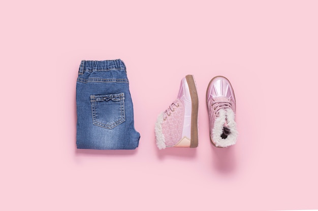 Boots and blue jeans for a girl on a pink background. Top view, flat lay.