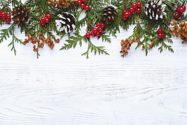 Border of Christmas tree branches pine cones flowers berries on white wooden background copy space