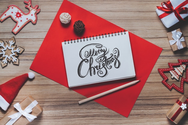 Border of new year decorations and gifts on wooden background with Merry Christmas wishes written with calligraphic font at the opened notebook