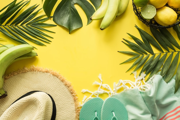 Border of outfit beach female accessories. Tropical vacations, straw sun hat, towel, monstera leaves on yellow. Summer concept.