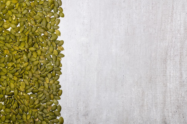 Border of peeled pumpkin seeds on a gray concrete background copy space