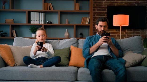 Bored child girl resting at home with father young dad using mobile phone family cellphone addiction