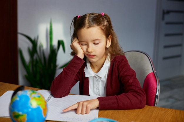 Bored schoolgirl sit at desk doing homework reading homeschooling