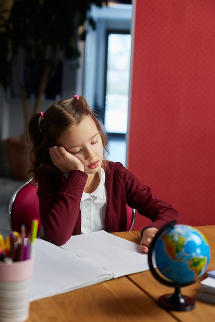 Bored schoolgirl sit at desk doing homework reading homeschooling