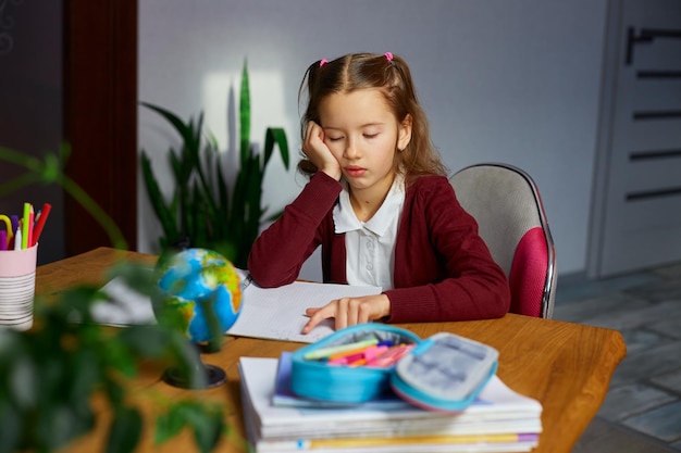 Bored schoolgirl sit at desk doing homework reading homeschooling