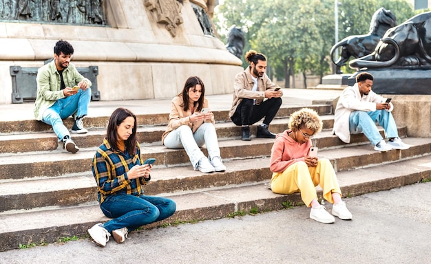 Bored students group using mobile smart phone sitting at university college yard