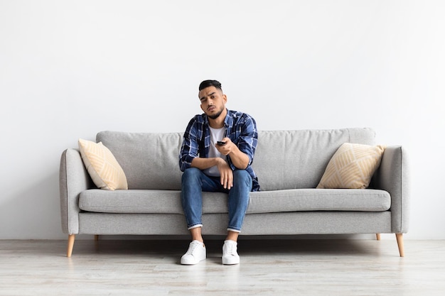 Bored young man watching television sitting on couch