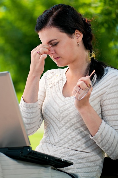 Bored young woman working with laptop in summer park Businesswoman under stress outside