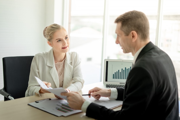 Boss businessman talking seriously about report with woman employee at desk in office