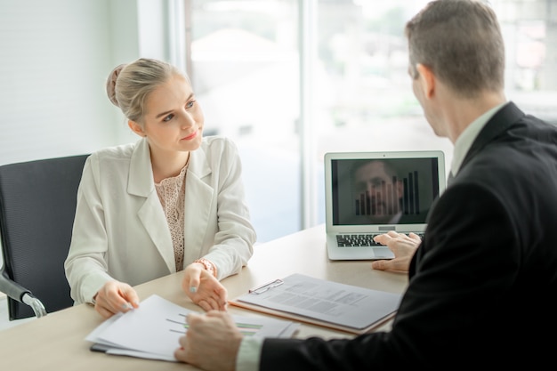 Boss businessman talking seriously about report with woman employee at desk in office