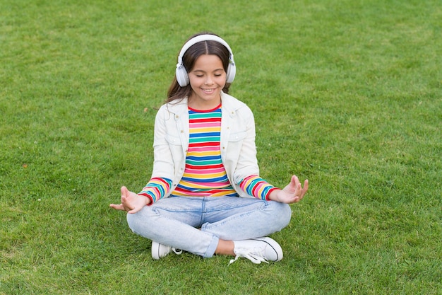 Do not bother me Cool girl headphones listening music Educational podcast Listen music while relaxing outdoor Kid girl enjoy music green grass meadow Pleasant time Child headphones listen music