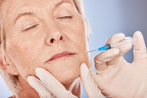 Botox cosmetics and senior woman with a beautician doing an anti aging treatment in a studio Beauty skincare and elderly lady doing cosmetic filler injection for facial wrinkles by gray background