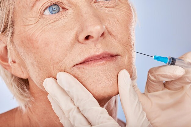 Botox injection and antiaging with a senior woman in studio on a gray background with hands in gloves for treatment Wrinkles wellness and cosmetics with a mature female patient and plastic surgeon