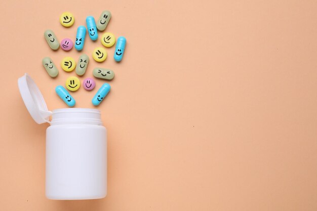 Photo bottle and antidepressant pills with funny faces on pale orange background flat lay space for text