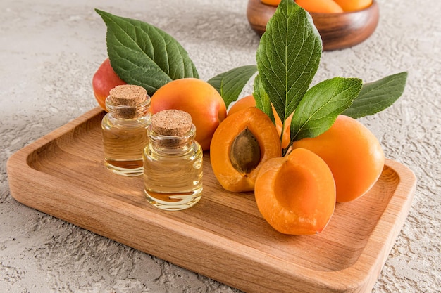 Bottle of apricot kernel oil on a wooden tray with ripe fruit and a gray cement background organic skin care