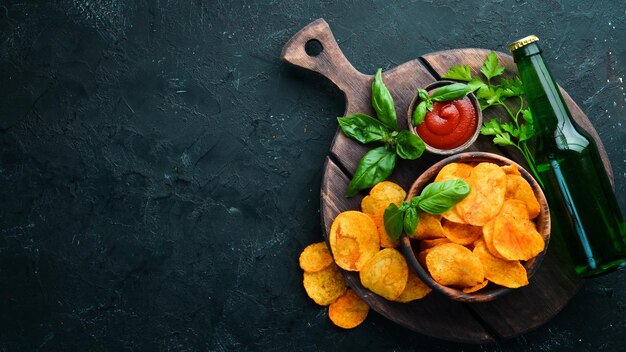 A bottle of beer and Potato chips with spices on a black background Snacks to beer Top view Free space for text