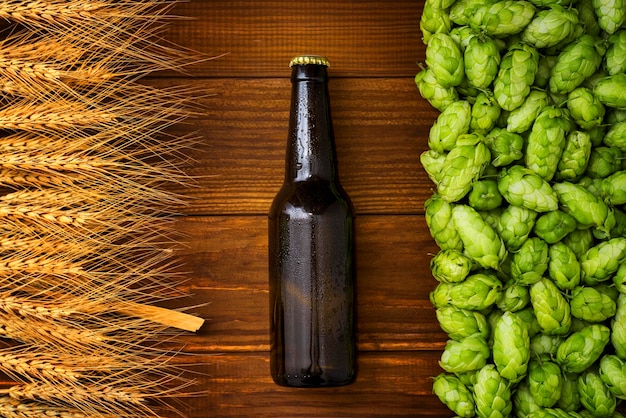 A bottle of beer on a wooden background with green hops and wheat ears