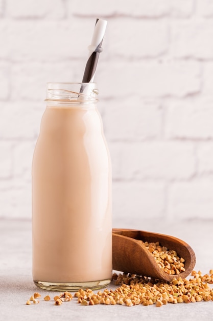 A bottle of buckwheat milk and raw buckwheat on a light background.