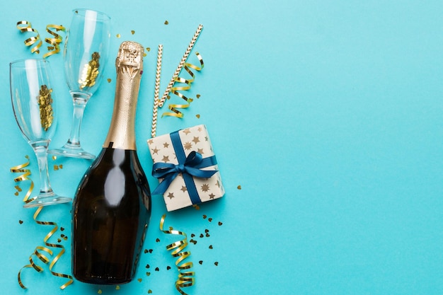 Bottle of champagne with colored glitter confetti and gift box space for text on colorfull background top view Hilarious christmas and birthday celebration