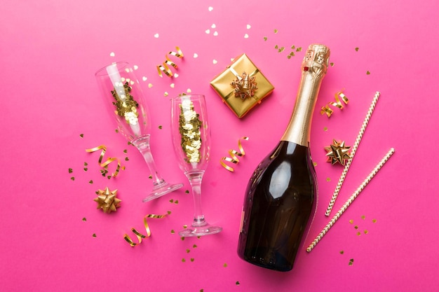 Bottle of champagne with colored glitter confetti and gift box space for text on colorfull background top view Hilarious christmas and birthday celebration