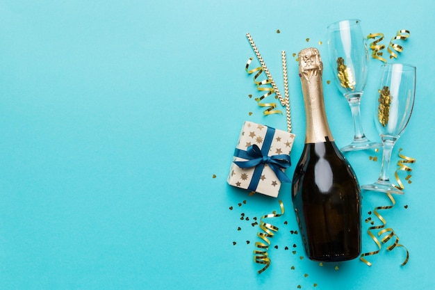 Bottle of champagne with colored glitter confetti and gift box space for text on colorfull background top view Hilarious christmas and birthday celebration