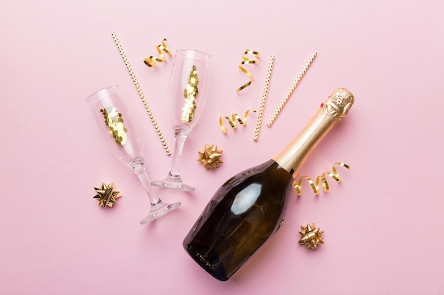 Bottle of champagne with glasses and colorful confetti on colored background. top view flay lay.