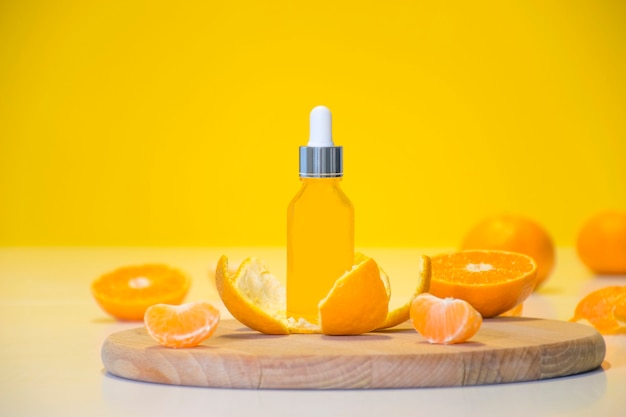 Bottle citrus essential oil in tangerine peel with orange pieces on yellow background with copy space.