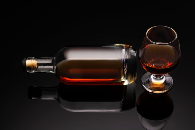 A bottle of cognac and a glass on a dark background