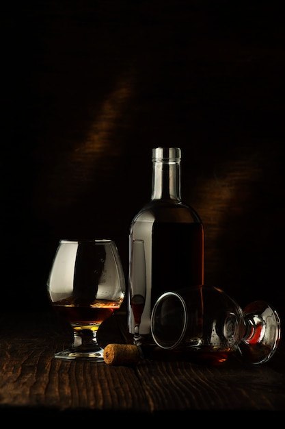 A bottle of cognac and two glasses on a dark wooden.