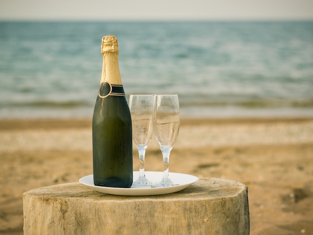 A bottle of cold champagne glasses and strawberries on a sandy beach.