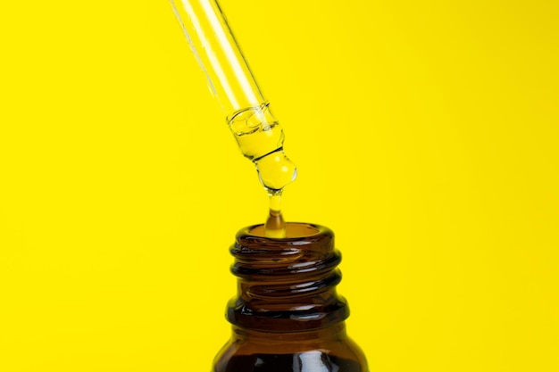 Bottle of cosmetic oil with a pipette on a yellow background Close up liquid drop dripping Beauty medicine and health care concept Macro photo Natural eco cosmetics