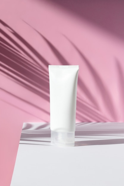 Bottle of cream with palm leaf shadow on pink surface