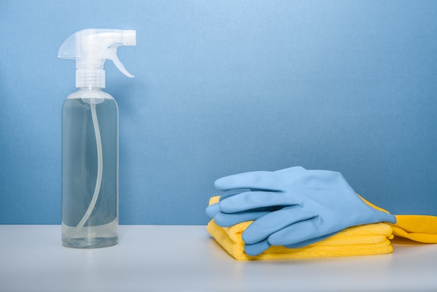 A bottle of detergent, protective gloves and microfiber cloths on blue background.