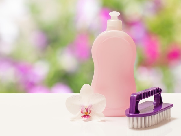 Bottle of dishwashing liquid and brush on blurred background