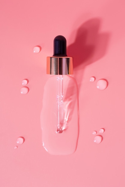 Bottle of drops of antiaging emulsion and glass pipette on light pink surface close upper view