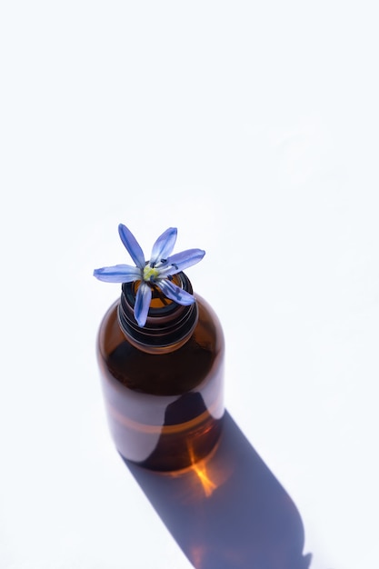 Bottle for essential oil with sharp shadow on a blue background. Essential oil bottle with blue snowdrop flower on top.