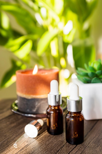 Bottle of essential oils with lighted candle on wooden table