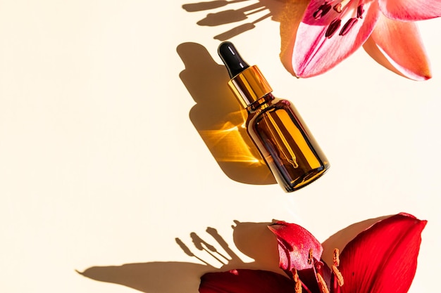 Bottle for the face in a glass bottle with a dropper on a beige background in the rays of the sun and a lily flower top view a copy of the space