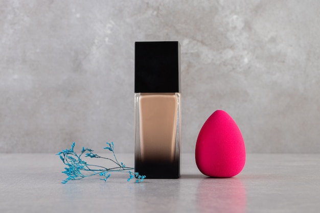 Bottle of foundation and pink makeup sponge on a stone table.