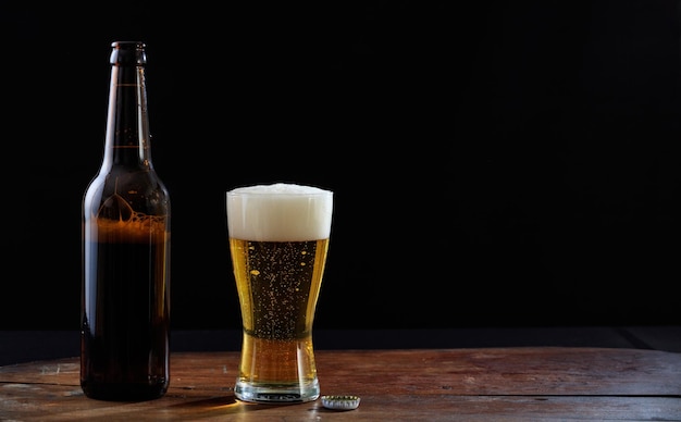 A bottle and a glass of beer on a wooden table dark background