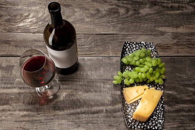 A bottle and a glass of red wine with fruits over wooden background