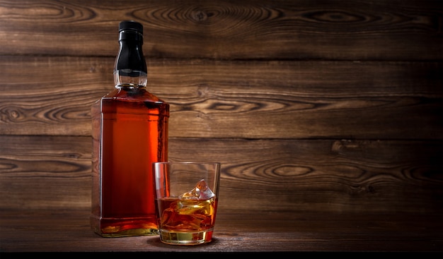 Bottle and glass of whiskey on wooden background