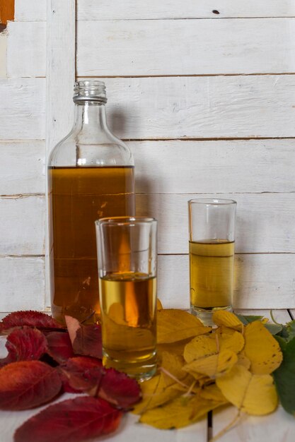 Photo bottle and glasses of brandy on the background of autumn leaves